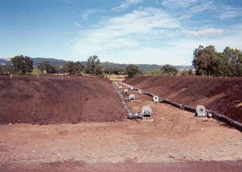 Upper Valley Disposal Service (Napa, CA). A good illustration of a very large Extended Aerated Static Pile System. Each pile (there are two shown) measures 550-feet long x 85-feet wide x 12-feet tall (~20,000 cubic yards each). The composting process for each pile is managed by 10-blowers operated by a programmable logic controller (PLC). This was a project that converted to an EASP system from a turned windrow system and reduced the overall footprint of the active composting area by 75 percent. In the early 1990s, this facility was on the verge of being closed down due to odor impacts to neighbors. With EASP Composting, the facility is still operating nearly 24 years later.